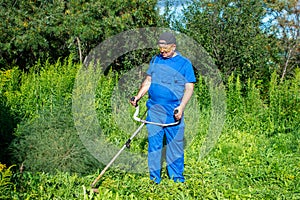 Man in a blue jumpsuit mowing the grass with a trimmer.