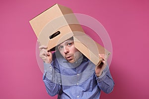 Man in blue shirt with a brown paper box on his head, hiding from job stress.