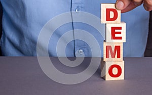 A man in a blue shirt composes the word DEMO from wooden cubes vertically photo