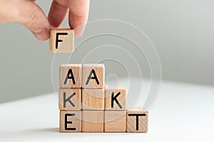 A man in a blue shirt composes the word FAKE from wooden cubes vertically