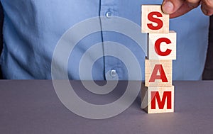 A man in a blue shirt composes the word SCAM from wooden cubes vertically photo