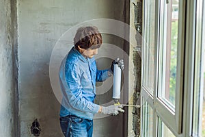 Man in a blue shirt does window installation. Using a mounting foam