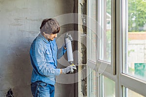 Man in a blue shirt does window installation. Using a mounting foam