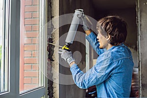 Man in a blue shirt does window installation. Using a mounting foam