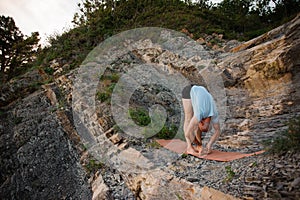 Man in blue shirt doing second step of surya namaskar, uttanasana forward bending pose