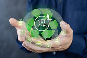 A man in a blue shirt holds a green recycling symbol with the words net zero. The recycling symbol has a plant on it, suggesting