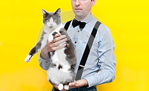 Man in blue shirt with long sleeves and black suspender and bow tie holding adorable grey and white cat with outstretched paws