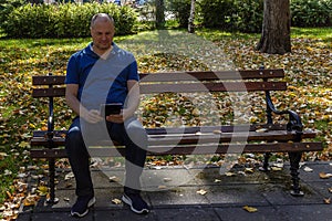 Man in blue shirt reading with digital tablet on a park bench