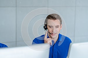 Man in blue shirt uniform working care customer service wearing headphone talking with customer at call center office