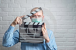 Man in blue shirt in virus mask on white with clapperboard