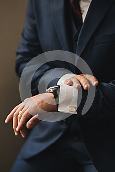 A man in a blue stylish suit looks at his watch. Hands close-up with manteds and gold cufflinks