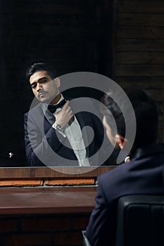 Man in blue suit and butterfly sitting in chair looking in the mirror in barbershop