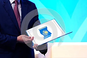 A man in a blue suit holds an open folder with the image of the national flag of the Republic of Kazakhstan. The concept of awardi