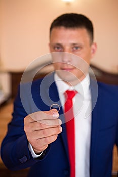 A man in a blue suit with a red tie holds an wedding ring