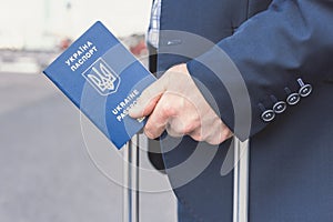 Man in a blue suit with a suitcase and a ukrainian passport at the airport. Business trip concept.