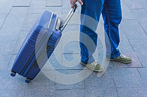 A man with a blue suitcase on wheels waiting for transport