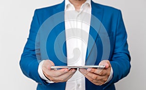 Man in the blue suite and white shirt holds mobile phone in the hand. Business concept with businessman and mobile phone