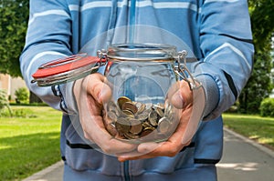 Man in blue sweatshirt holding money jar with coins