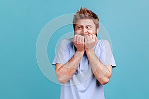 Man in blue T-shirt biting nails, nervous about troubles, panicking and looking scared.