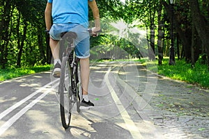 Man in blue t-shirt and blue jeans shorts cycling in the nature on bicycle on outdoor trail in park