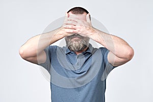 Man in blue t-shirt covering his face with hands