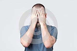 Man in blue t-shirt covering his face with hands
