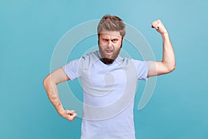 Man in blue T-shirt demonstrating power in his hands, showing biceps, feeling energy to win success.