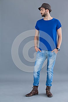 Man in blue t-shirt and fedora hat posing with hands in his pockets