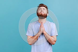 Man in blue T-shirt folding hands in pray looking up, communicating with god, asking for forgiveness
