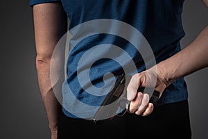 A man in a blue T-shirt pulls a gun behind his back