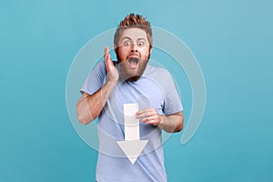 Man in blue T-shirt showing white arrow pointing down expressing shocked emotions, downgrade concept