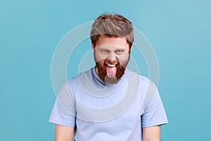 Man in blue T-shirt with tongue out mouth, having childish and naughty facial expression.