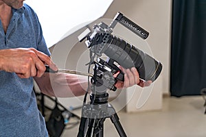 A man in a blue t-shirt tuns up a professional camera for work on the background of studio