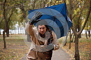 Man with blue umbrella caught in gust of wind outdoors