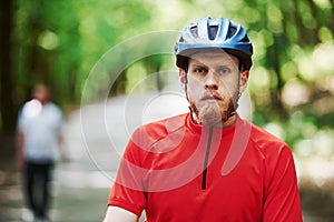 Man in blurred background. Cyclist on a bike is on the asphalt road in the forest at sunny day