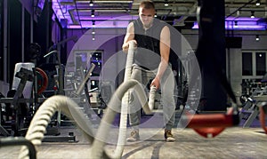 Man bodybuilder doing exercise using battle ropes