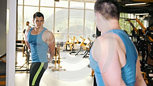 Man bodybuilder posing and shows muscles near mirror in the gym