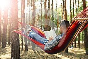 Man with book relaxing in hammock outdoors on summer day