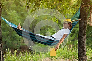 Man with book resting in comfortable hammock at green garden