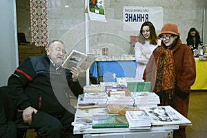 Man bookseller reading book selling it to women customers, bookstore counter. Book Fair. Kyiv, Ukraine