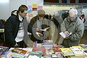 Man bookseller selling books to two old men, bookstore counter. Book Fair. Kyiv, Ukraine