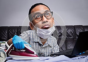 Man with boring face working with very busy business and housework part, ironing, working with laptop during self isolation