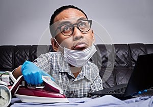 Man with boring face working with very busy business and housework part, ironing, working with laptop during self isolation photo