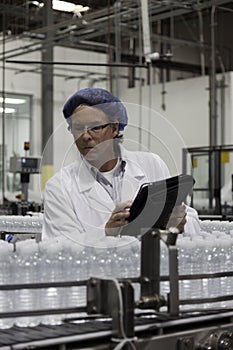 Man at bottling plant inspecting bottled water on conveyor