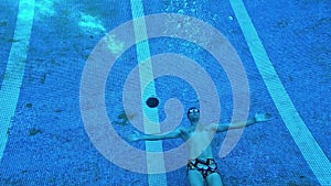 A man at the bottom of a blue pool releases round bubbles from the air