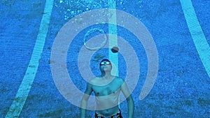 A man at the bottom of a blue pool releases round bubbles from the air