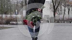 man with bouquet roses behind his back street slowly walks waits meeting