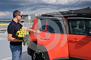 A man with a bouquet of yellow roses opens the door of his car in the parking lot. Travel concept