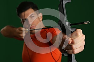 Man with bow and arrow practicing archery against green background, focus on hand