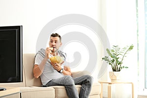 Man with bowl of potato chips watching TV on sofa